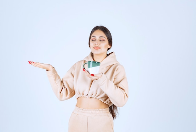 Young woman with a green mug pointing at somewhere on the left