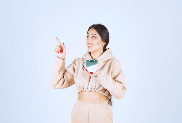 Young woman with a green mug pointing at somewhere on the left