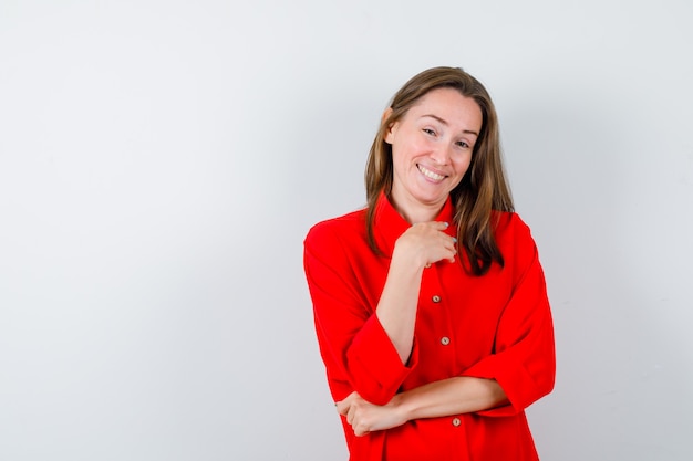 Young woman with hand on chest in red blouse and looking happy , front view.