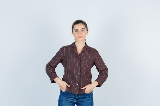 Young woman with hands in pockets in striped shirt, jeans and looking happy , front view.