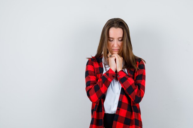 Young woman with hands in praying gesture in casual clothes and looking hopeful , front view.