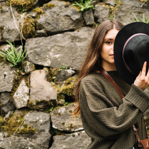 Young woman with hat in front of natural wall