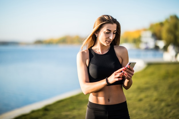 秋の自然の中でジョギングし、携帯電話を探しているヘッドフォンを持つ若い女性