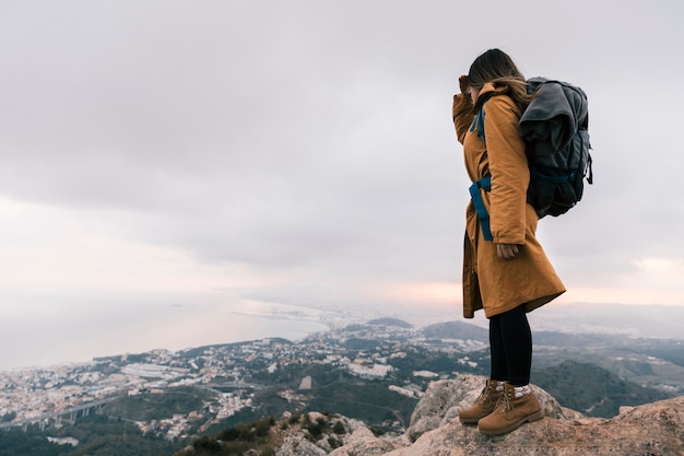 Young woman with her backpack standing on the top of mountain looking at idyllic view