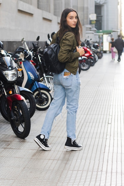 歩道を歩いて彼女のバックパックを持つ若い女