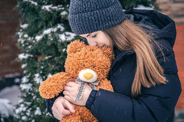 Young woman with her favorite teddy bear in her arms in winter