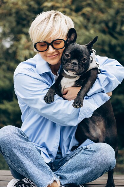 Young woman with her pet french bulldog sitting on a bench in a park