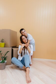 A young woman with her son is sitting in front of the boxes and rejoicing at the housewarming after moving in. housewarming, delivery and freight transportation, purchase of real estate.