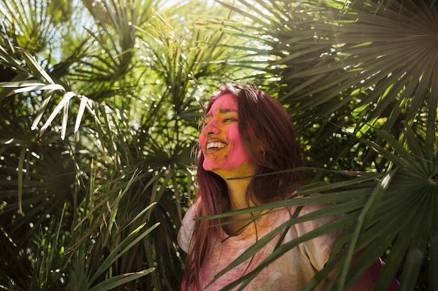 Giovane donna con colore holi sul suo viso in piedi vicino alla pianta verde