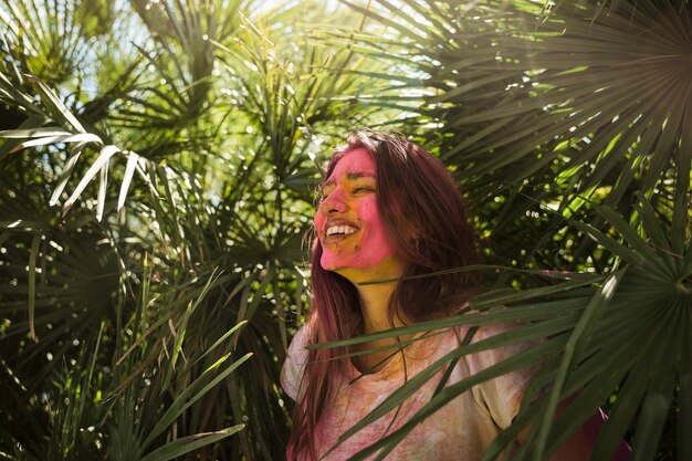 녹색 식물 근처에 서있는 그녀의 얼굴에 holi 색깔을 가진 젊은 여자