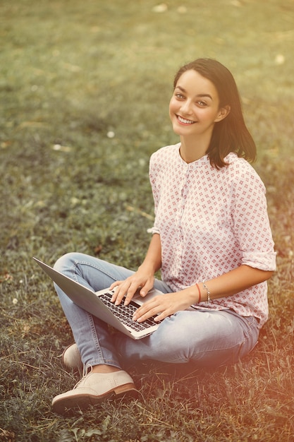 Young woman with laptop sitting on green grass