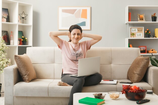 Young woman with laptop sitting on sofa behind coffee table in living room