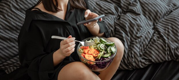 ベッドに野菜と新鮮なサラダの大きなボウルを持つ若い女性。