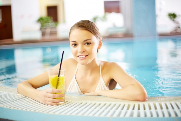 Young woman with a lemonade in the swimming pool