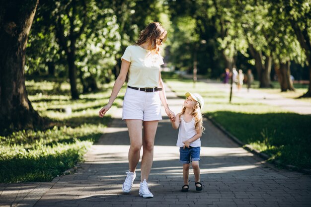 公園を歩いて小さな娘を持つ若い女性