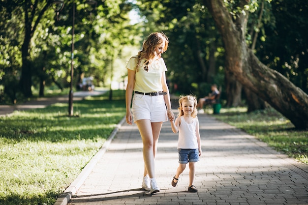 公園を歩いて小さな娘を持つ若い女性