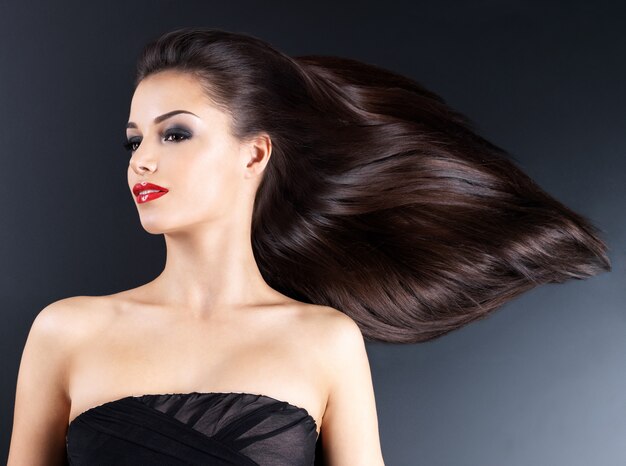 Young woman with long brown straight hairs on a dark wall