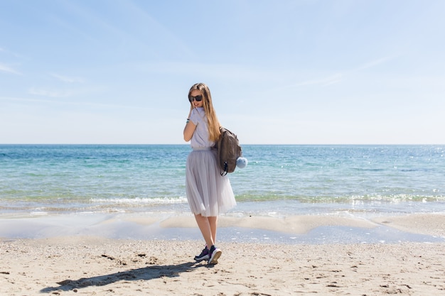 長い髪と海の近くの背中にバッグを持つ若い女性