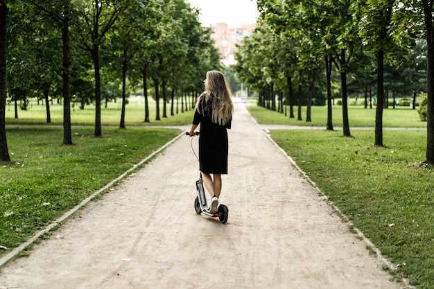Молодая женщина с длинными волосами на электрический скутер. Девушка на электрическом самокате.