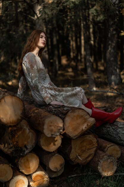 Young woman with long red hair in a linen dress gathering mushrooms in the forest 