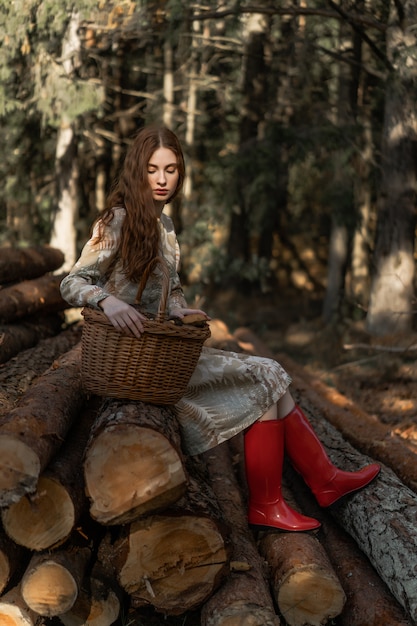 Young woman with long red hair in a linen dress gathering mushrooms in the forest