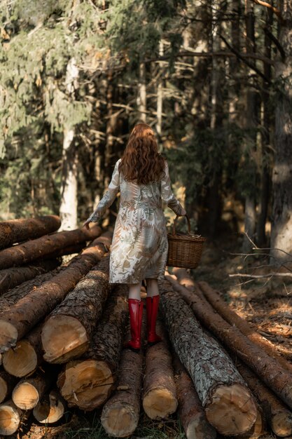 Young woman with long red hair in a linen dress gathering mushrooms in the forest 
