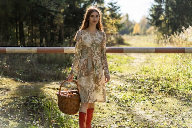 Young woman with long red hair in a linen dress gathering mushrooms in the forest 