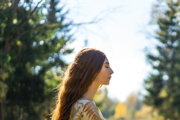 Young woman with long red hair in a linen dress gathering mushrooms in the forest 