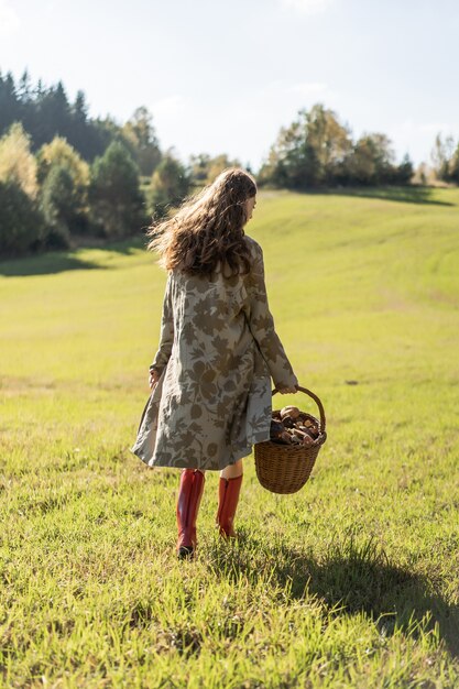 Young woman with long red hair in a linen dress gathering mushrooms in the forest 