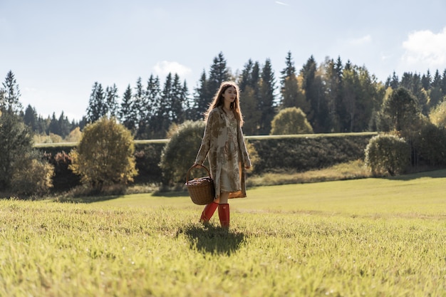 Young woman with long red hair in a linen dress gathering mushrooms in the forest