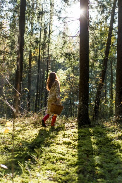 Young woman with long red hair in a linen dress gathering mushrooms in the forest 