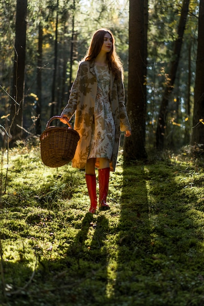 Young woman with long red hair in a linen dress gathering mushrooms in the forest 