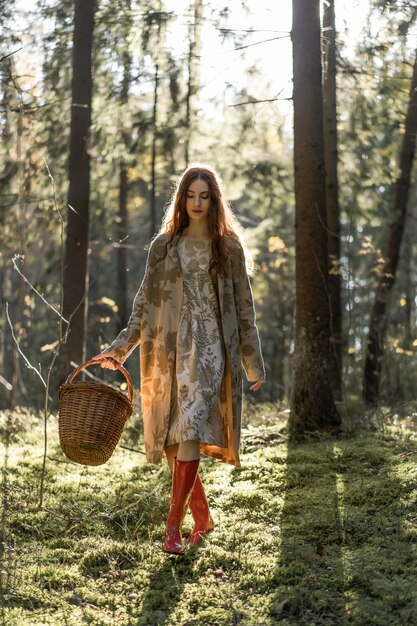 Young woman with long red hair in a linen dress gathering mushrooms in the forest