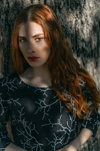 Young woman with long red hair in a linen dress in a natural location on the background 