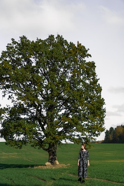 Free photo young woman with long red hair in a linen dress in a natural location on the background