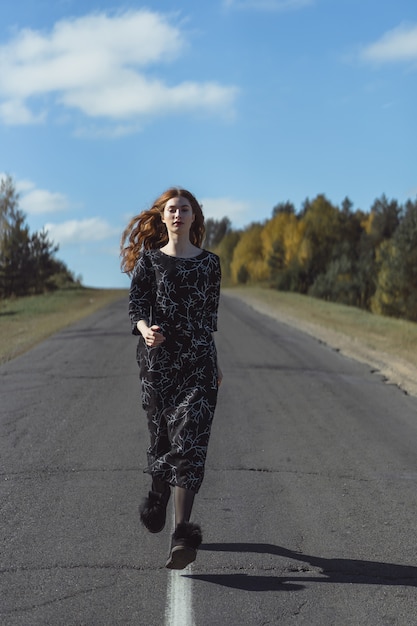 Young woman with long red hair in a linen dress in a natural location on the background 