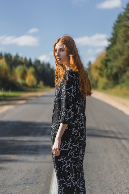 Young woman with long red hair in a linen dress in a natural location on the background 