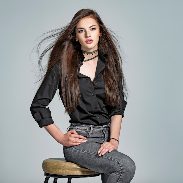 Young woman with long straight hair - at studio. Portrait of an attractive brunette girl. Fashion model wears black shirt anf jeans. Sexy female model
