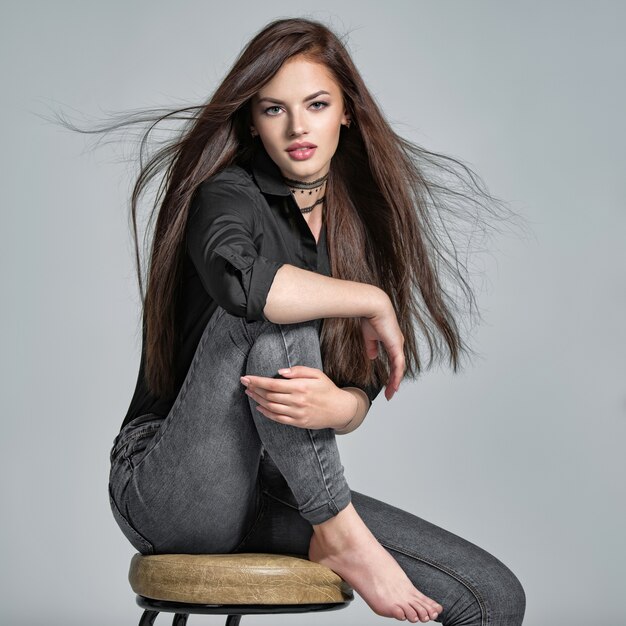 Young woman with long straight hair - at studio. Portrait of an attractive brunette girl. Fashion model wears black shirt anf jeans. Sexy female model