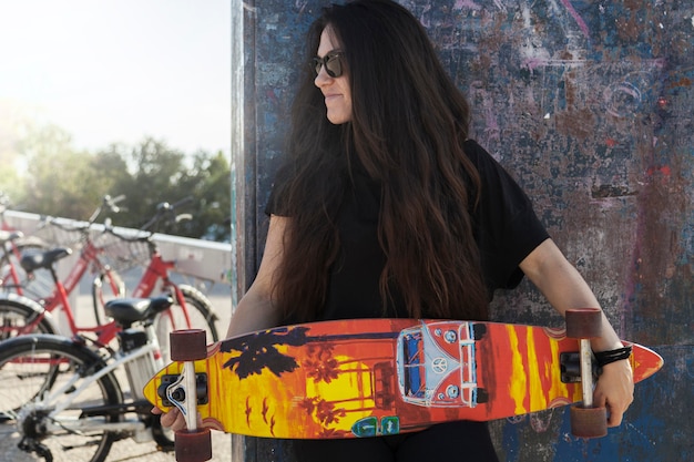 Free photo young woman with longboard near wall