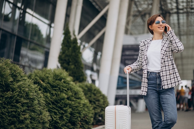 Giovane donna con bagagli in aeroporto che viaggia e parla al telefono