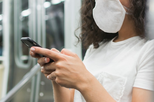Молодая женщина с медицинской маской, проверка ее телефон в метро