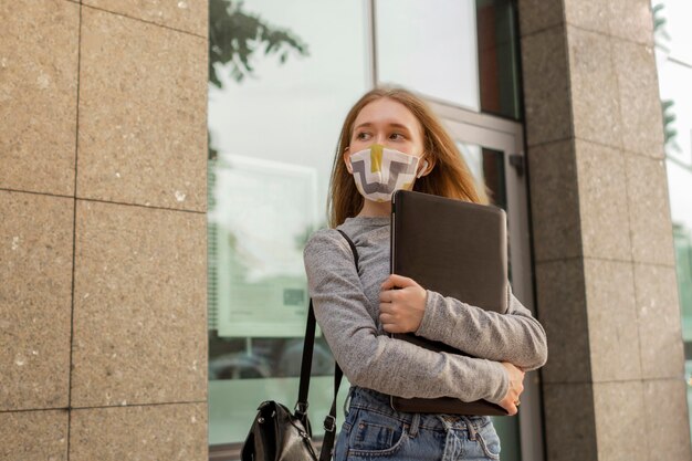 Young woman with medical mask holding her laptop outside