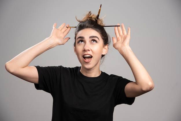 Young woman with messy bun standing on gray wall.