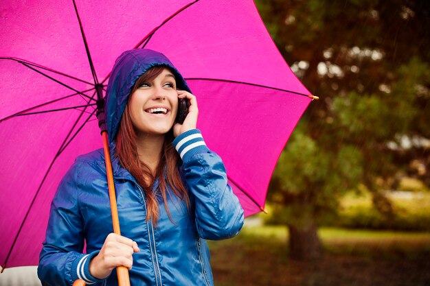 Молодая женщина с мобильным телефоном в дождливый день