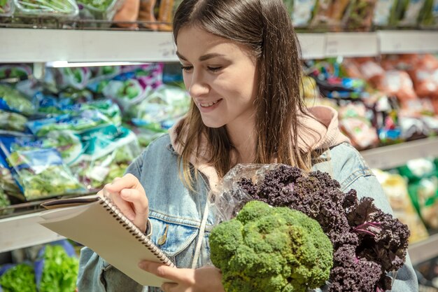 ノートを持った若い女性がスーパーで食料品を買う。