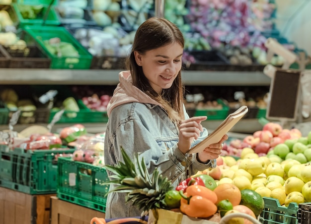 Молодая женщина с ноутбуком покупает продукты в супермаркете