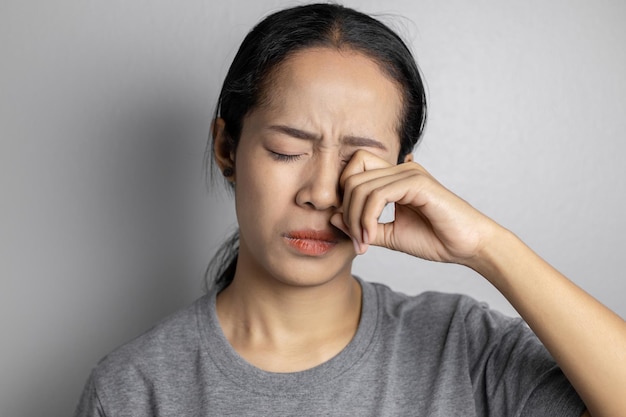 회색 배경에 눈 통증이 있는 젊은 여성. 아시아 여성은 눈 통증으로 고통 받고 있습니다. 심한 눈 통증으로 고통받는 여성.
