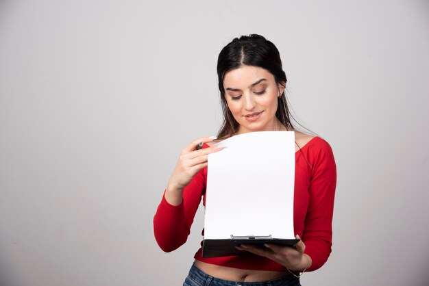 young woman with pen and clipboard on a gray background.