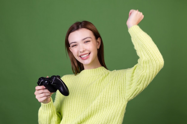 Foto gratuita giovane donna con trucco naturale perfetto marrone grandi labbra in maglione casual sulla parete verde con joystick che gioca ai videogiochi gesto vincitore